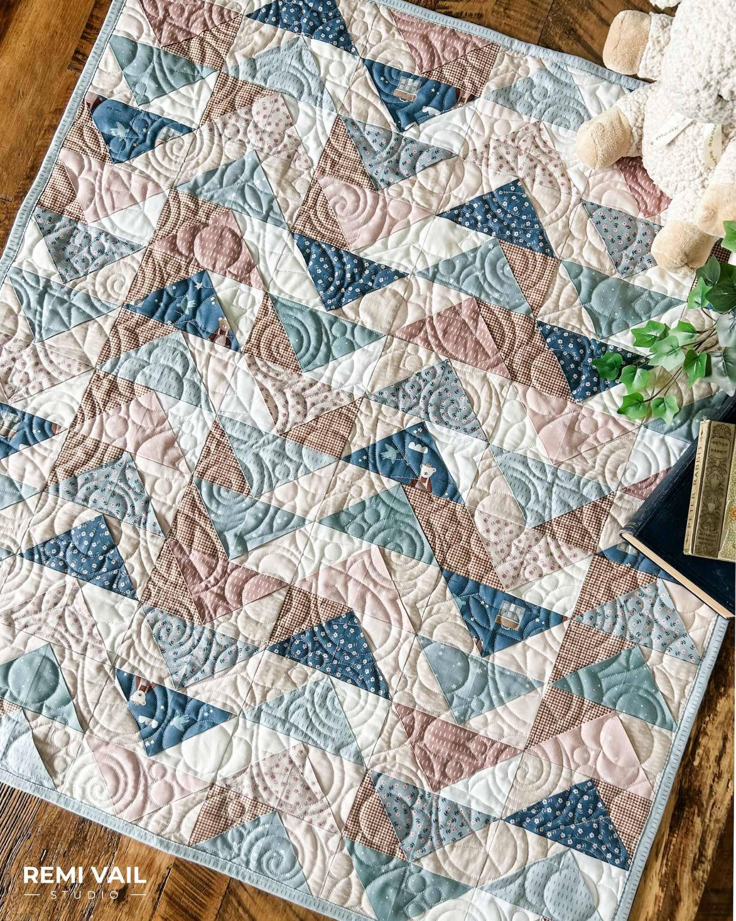 Front Porch Quilt made by Remi Vail Studio using the Cozy Bebe fabric collection by Riley Blake Designs. Quilt is lying on a wood floor with a stuffed animal, plant, and vintage books on top. 