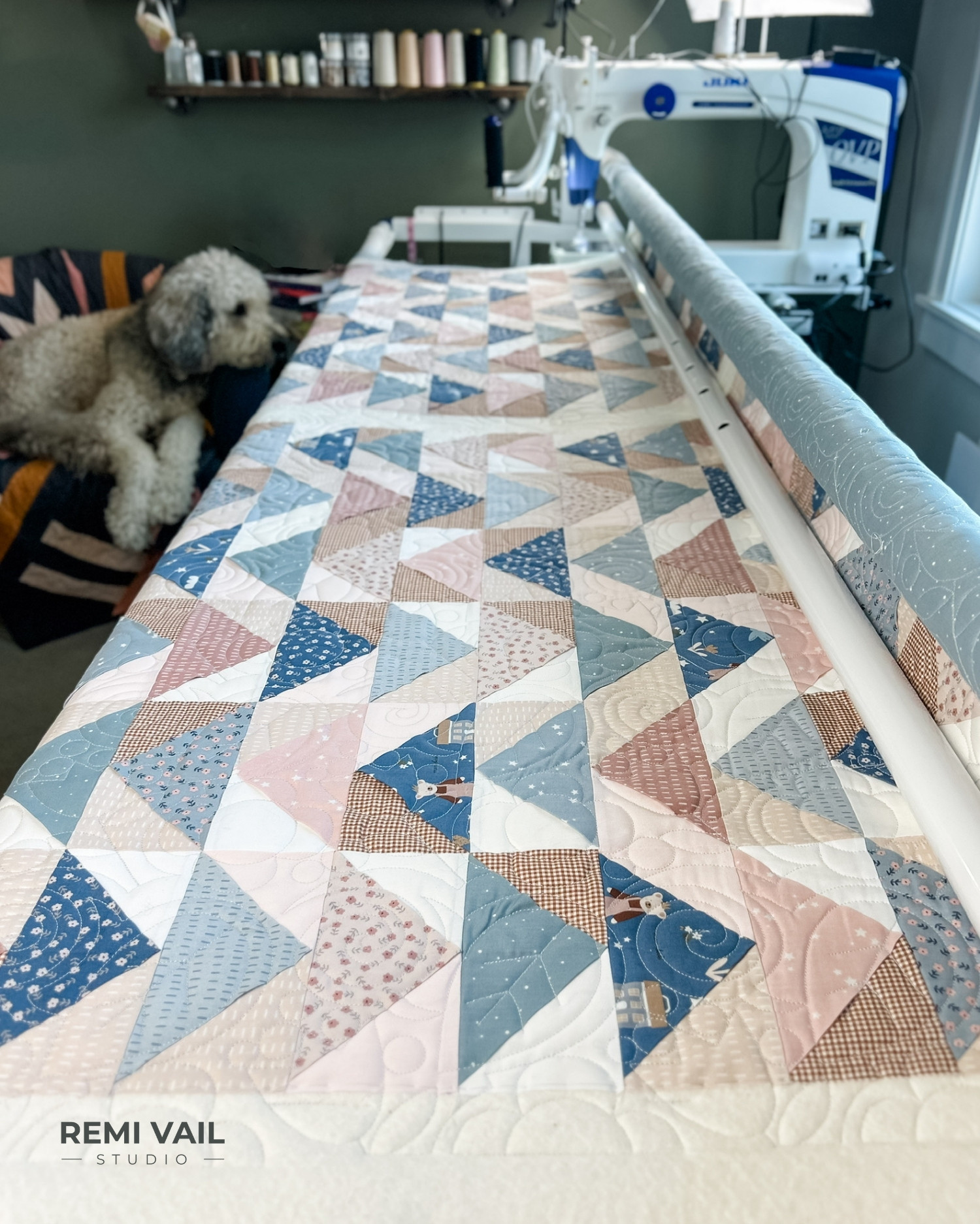Front Porch Quilt made by Tamara Darragh - Remi Vail Studio using the Cozy Bebe fabric collection by Riley Blake Designs. Quilting is being done on a Juki Myabi J350-QVP longarm. Corduroy the dog is in a chair next to the longarm. Quilt design is Cottage Core by Sew Shabby Quilting.