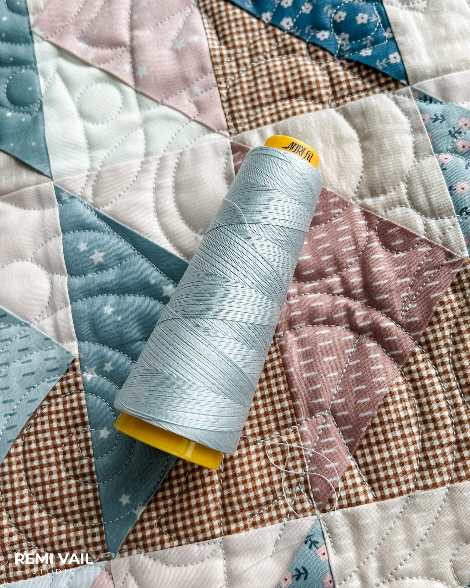Aurifil thread 40/3 weight spool on top of the Front Porch Quilt made by Tamara Darragh for Remi Vail Studio using the Cozy Bebe fabric collection for Riley Blake Designs.