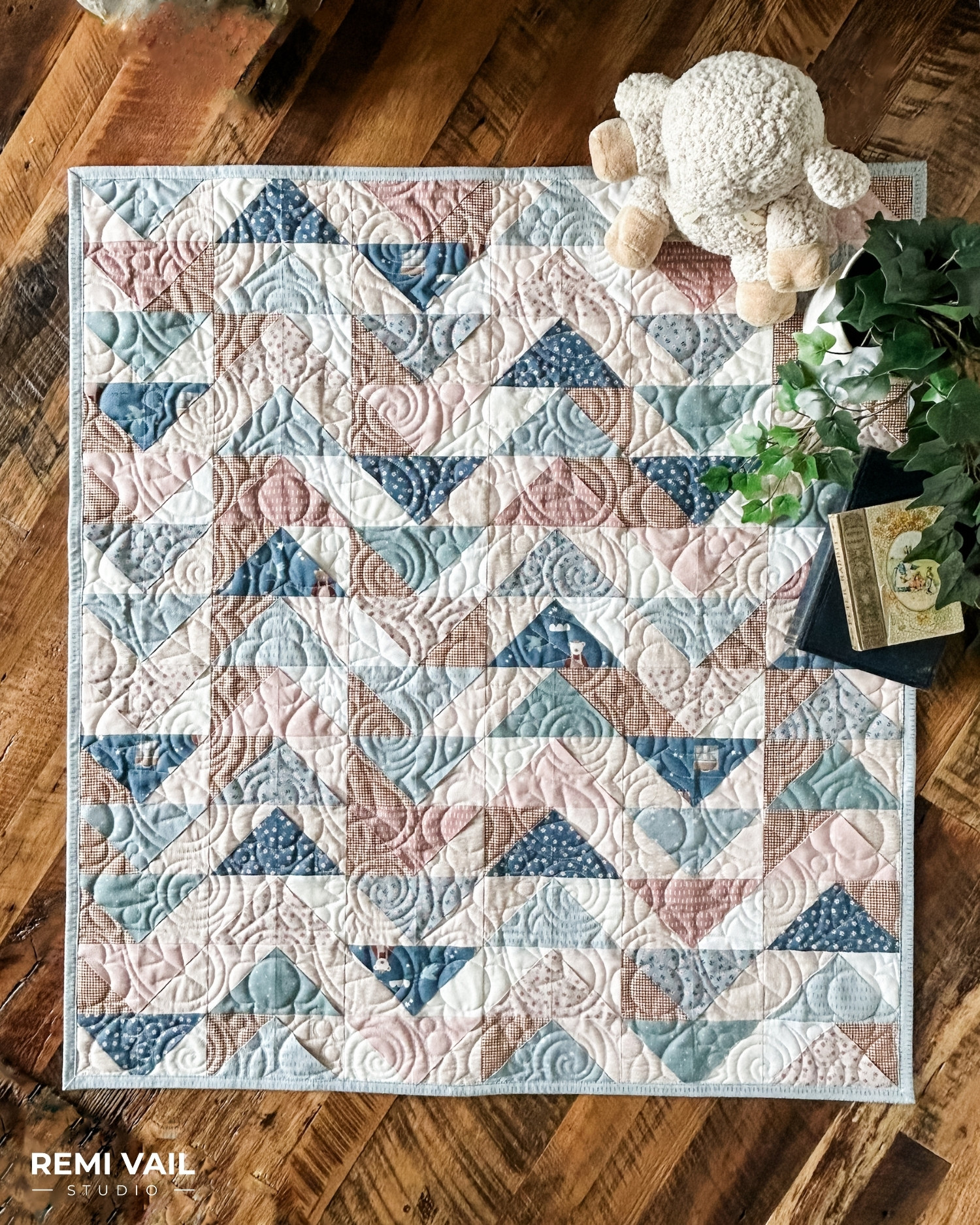 Front Porch Quilt made by Remi Vail Studio using the Cozy Bebe fabric collection by Riley Blake Designs. Quilt is lying on a wood floor with a stuffed animal, plant, and vintage books on top. 