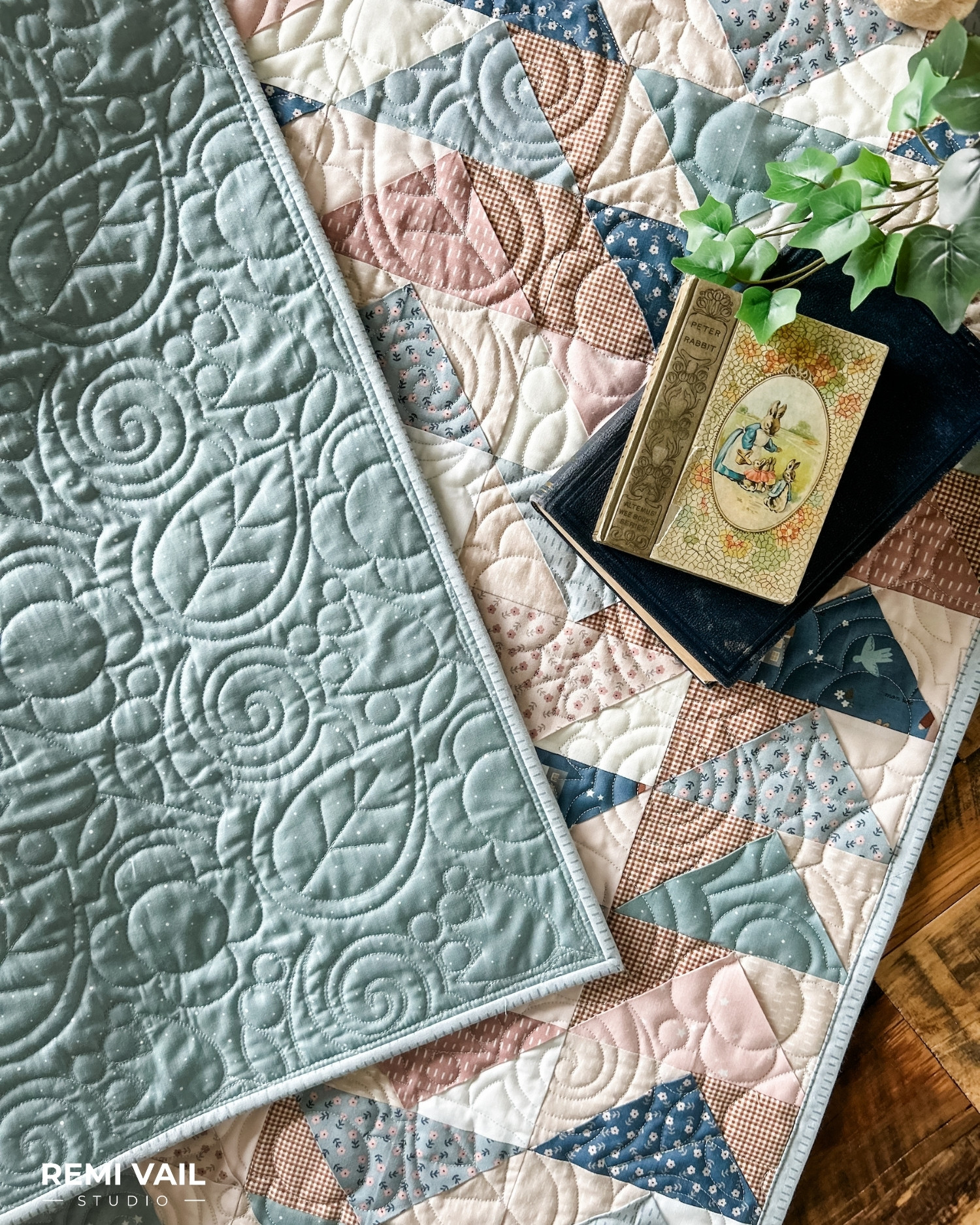 Front Porch Quilt made by Remi Vail Studio using the Cozy Bebe fabric collection by Riley Blake Designs. Quilt is lying on a wood floor with a plant, and vintage books on top. 