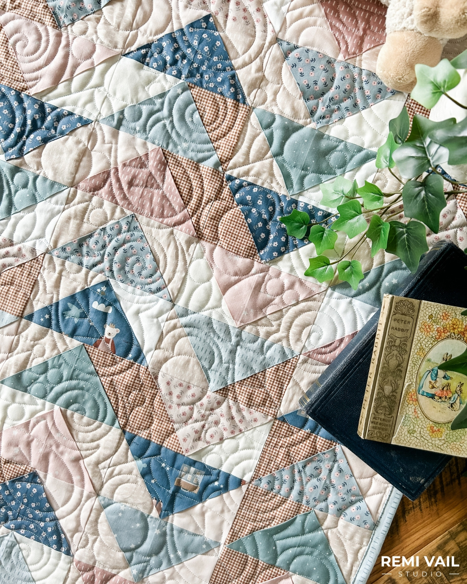 Front Porch Quilt made by Remi Vail Studio using the Cozy Bebe fabric collection by Riley Blake Designs. Quilt is lying on a wood floor with a stuffed animal, plant, and vintage books on top. 