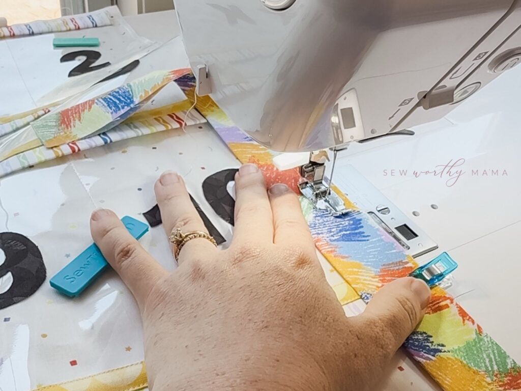 A process photo showing a sewing machine and hand as binding is sewn onto a project.