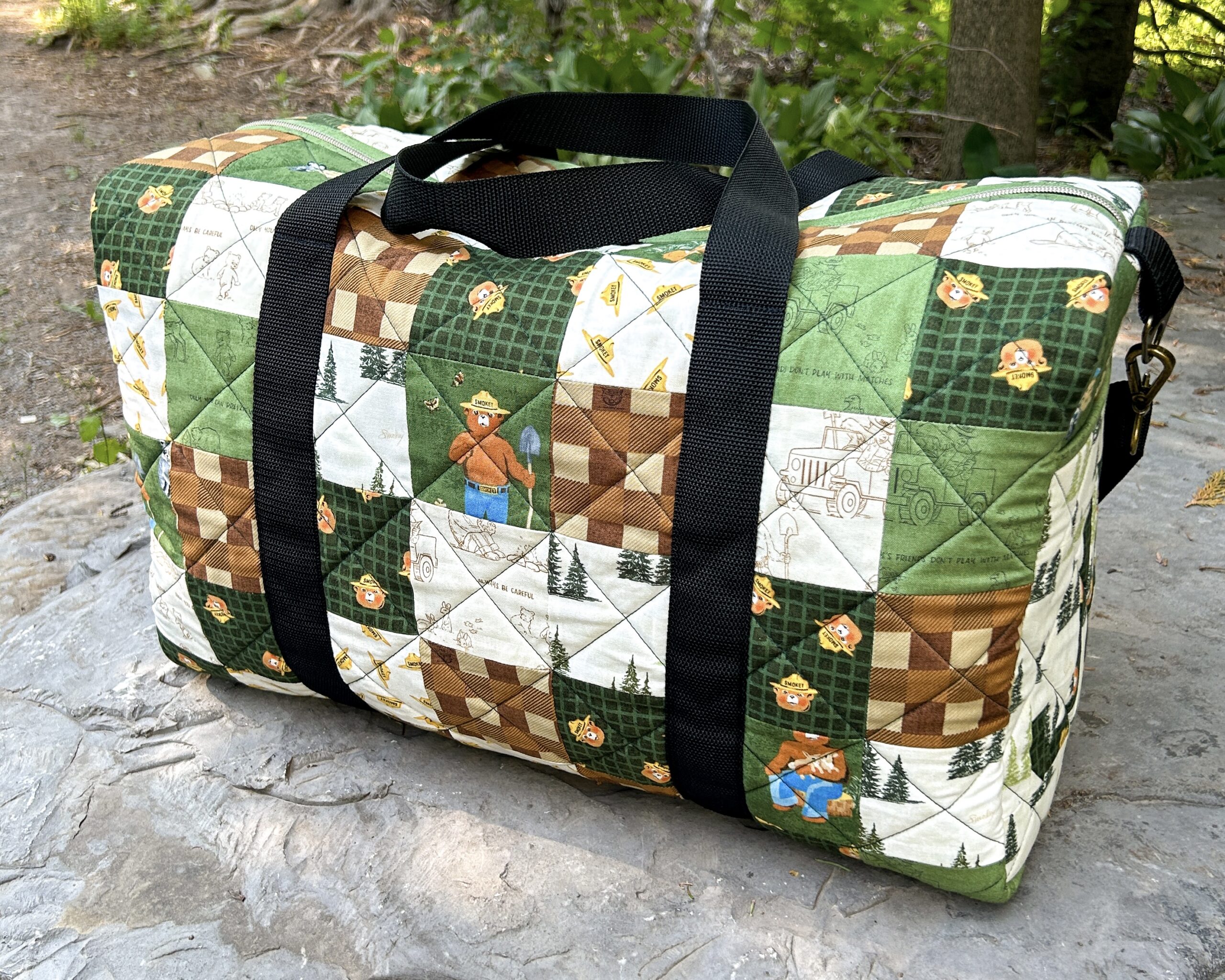 A completed patchwork duffle bag featuring bears and various fabrics, sit on a rock.