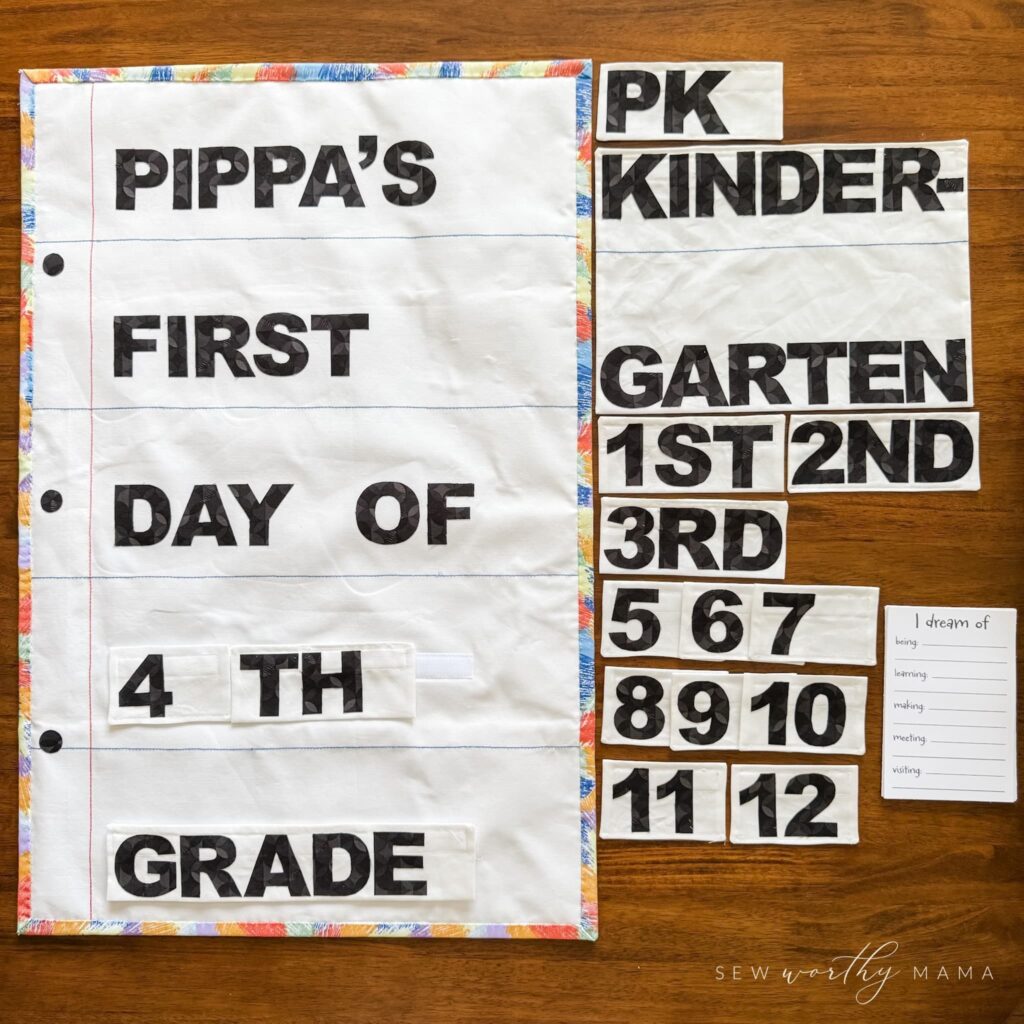 A flat lay showing a Pockets Full of Dreams first-day-of-school photo prop sign that says "Pippa's First Day of 4th Grade" next to an assortment of grade level labels and a stack of Dream Cards.
