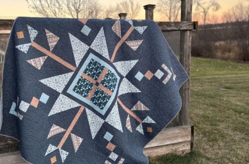 Lumi Quilt by Remi Vail Studio made by Tamara Darragh using the Winter Magic Fabric Collection designed by Dani Mogstad for Riley Blake Designs. The quilt is hanging on a garden fence at dusk.
