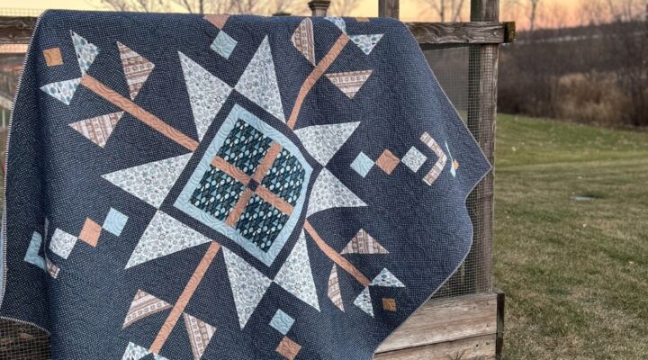 Lumi Quilt by Remi Vail Studio made by Tamara Darragh using the Winter Magic Fabric Collection designed by Dani Mogstad for Riley Blake Designs. The quilt is hanging on a garden fence at dusk.