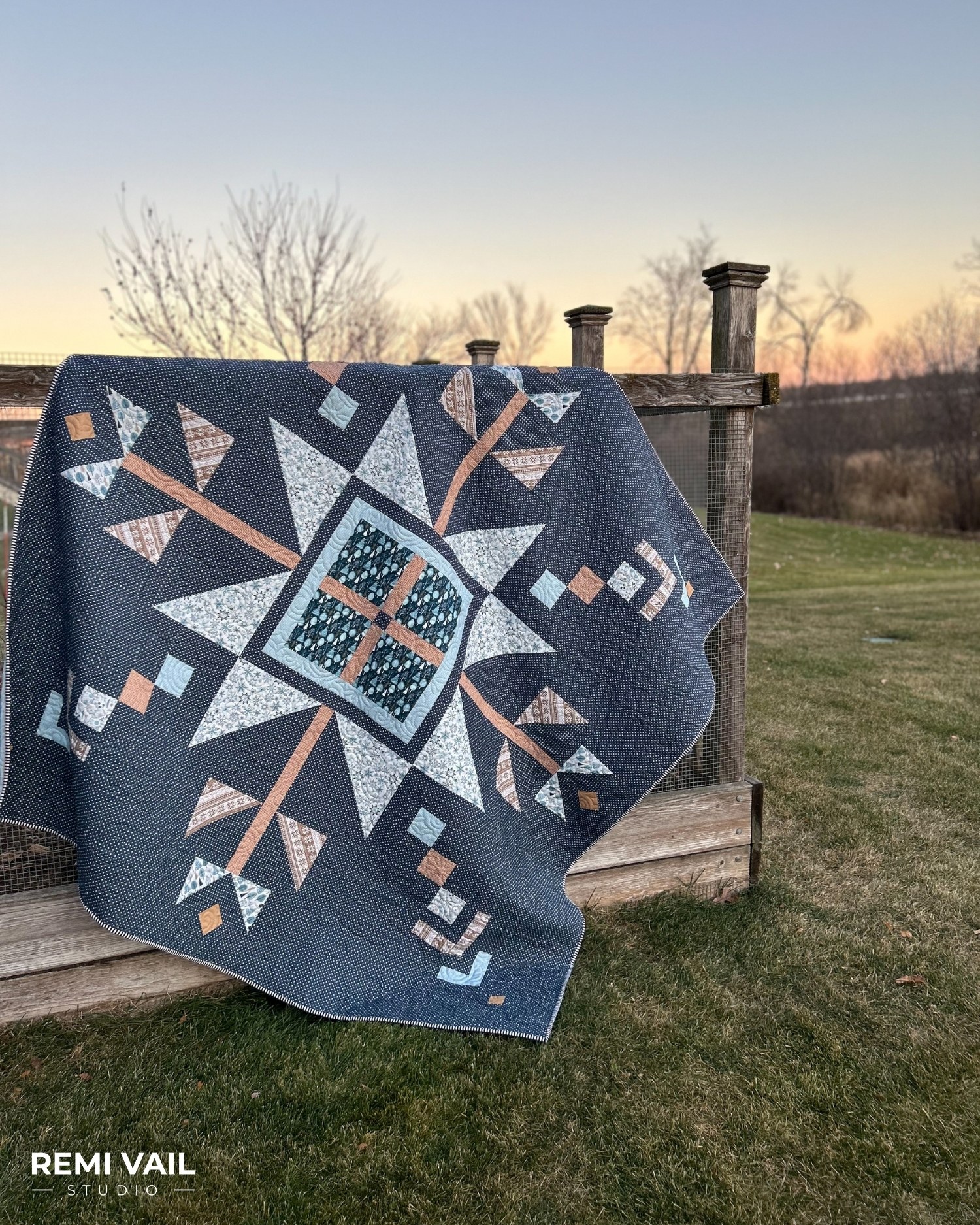 Lumi Quilt by Remi Vail Studio made by Tamara Darragh using the Winter Magic Fabric Collection designed by Dani Mogstad for Riley Blake Designs. The quilt is hanging on a garden fence at dusk.
