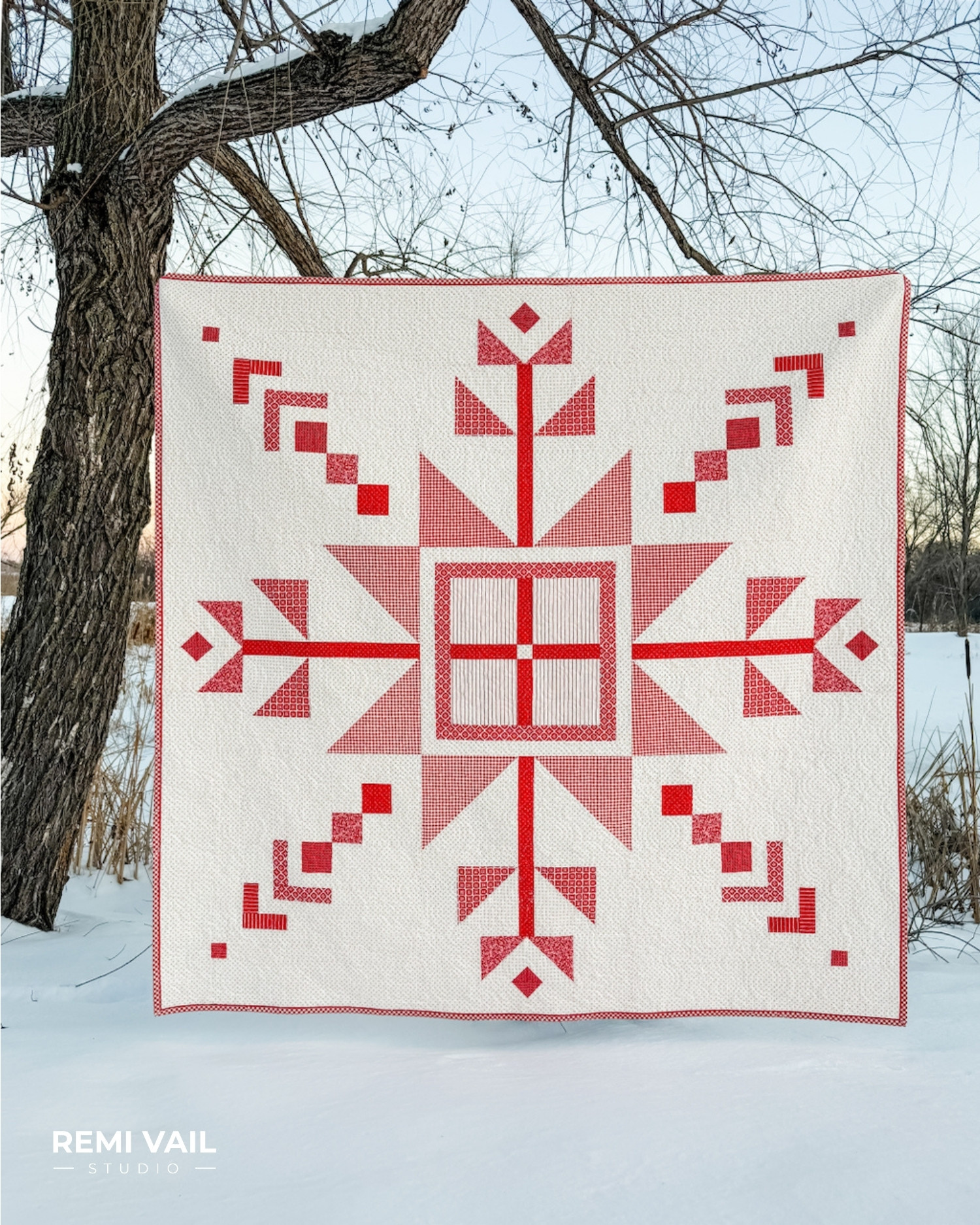 Lumi Quilt pattern by Tamara Darragh of Remi Vail Studio displayed outdoors in winter, featuring a red and white snowflake medallion made with the Radiant Ruby fabric collection by Riley Blake Designs.