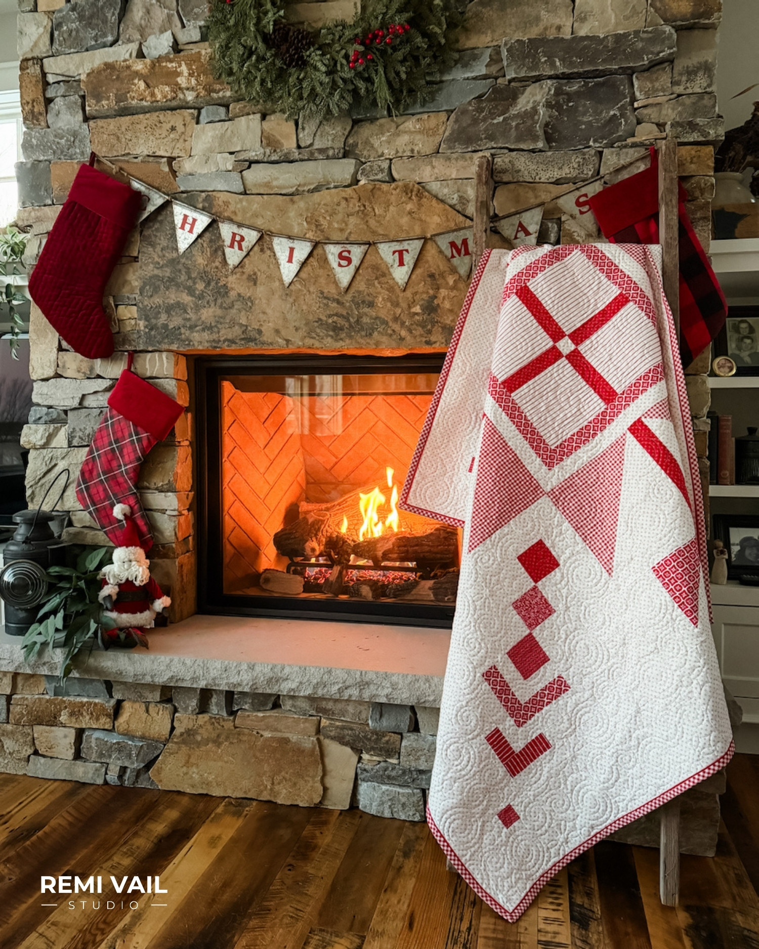 Lumi Quilt pattern by Tamara Darragh of Remi Vail Studio displayed indoors by a stone fireplace, featuring a red and white snowflake medallion made with the Radiant Ruby fabric collection by Riley Blake Designs.