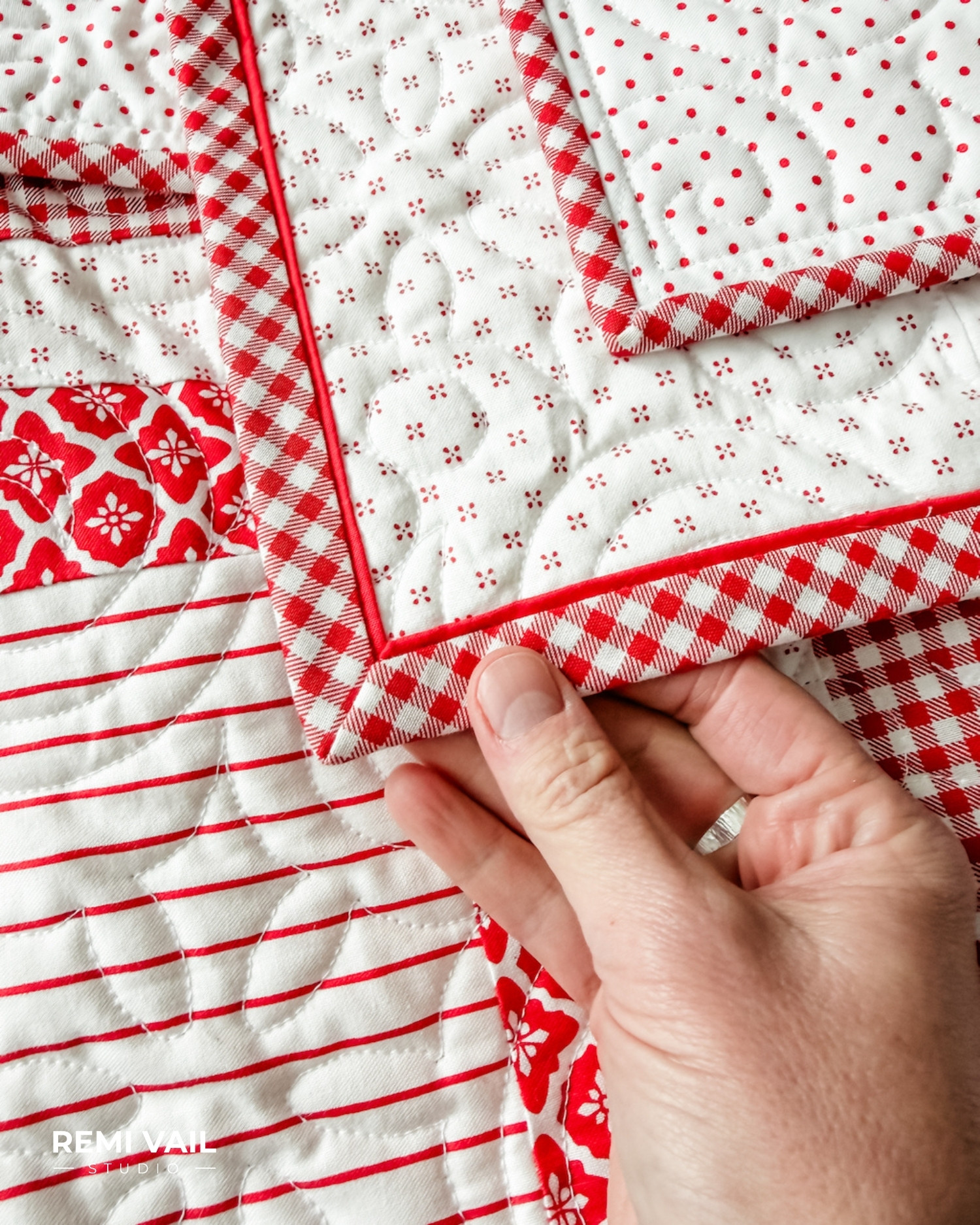 Hand holding a flange binding corner on the Lumi Quilt pattern by Tamara Darragh of Remi Vail Studio, made with red and white fabrics from the Radiant Ruby collection by Riley Blake Designs.