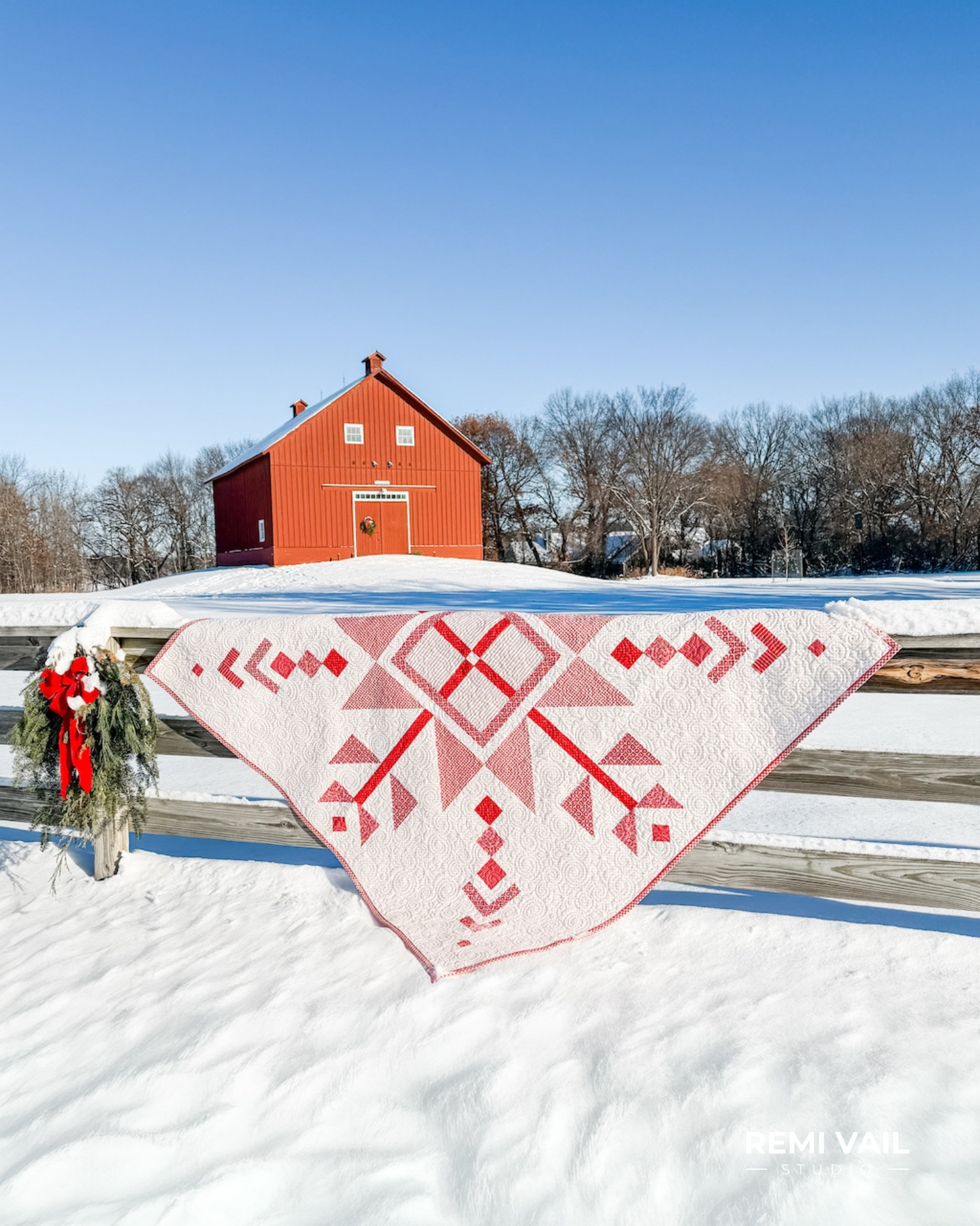 Lumi Quilt pattern by Tamara Darragh of Remi Vail Studio draped over a wooden fence in a snowy landscape, featuring a red and white snowflake medallion made with the Radiant Ruby fabric collection by Riley Blake Designs.