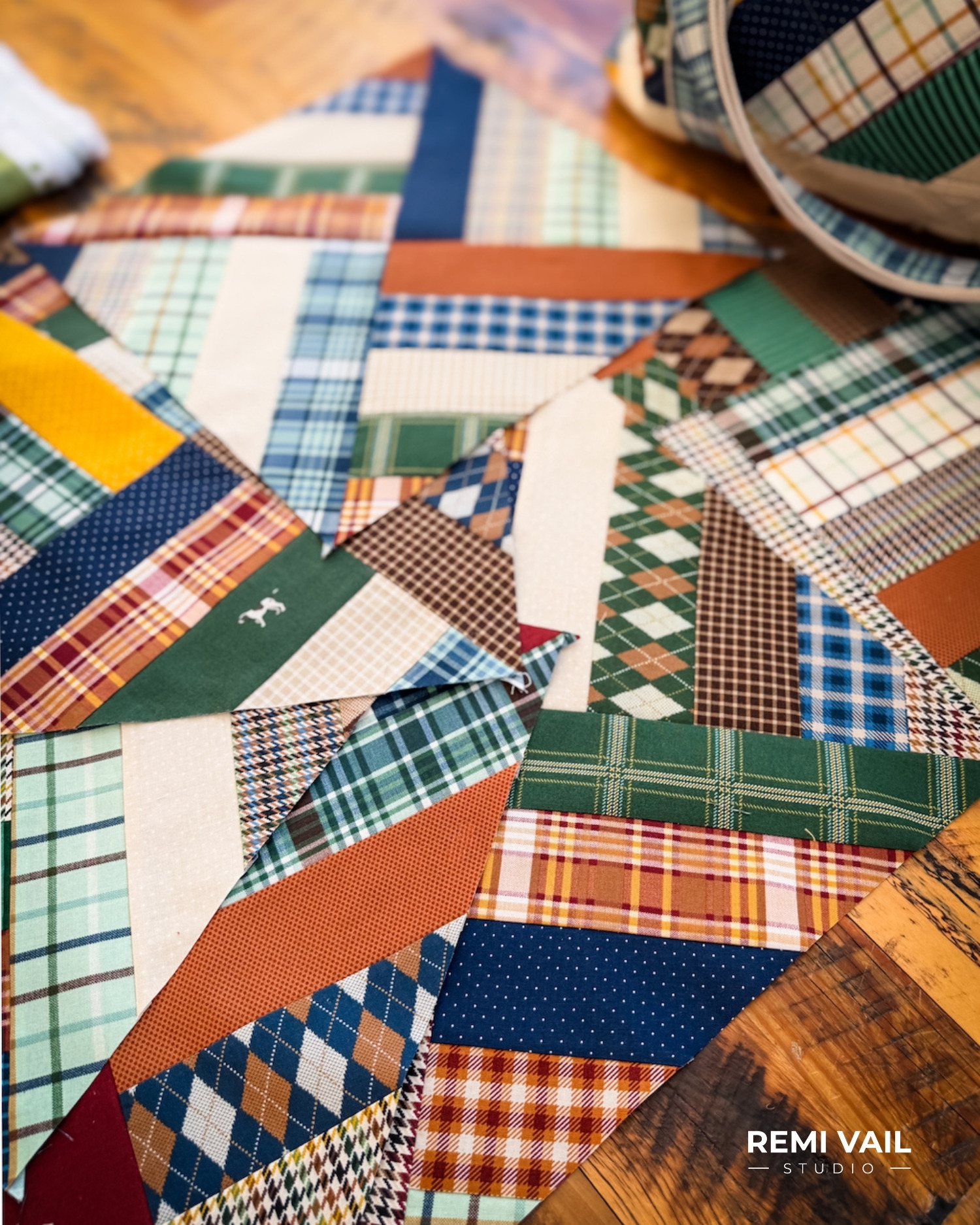 Quilt blocks from MEL's Quilt Pattern by Tamara Darragh of Remi Vail Studio spread out on the floor. The quilt blocks are made from a variety of fabric from the Plaid Venture Club collection by Riley Blake Designs.